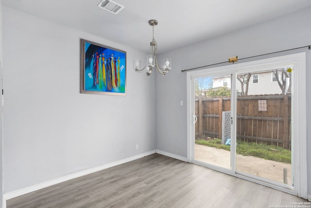 unfurnished dining area with a chandelier, visible vents, wood finished floors, and baseboards