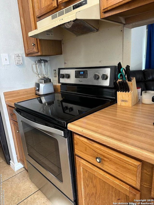 kitchen featuring wooden counters, brown cabinets, under cabinet range hood, stainless steel electric range oven, and light tile patterned flooring