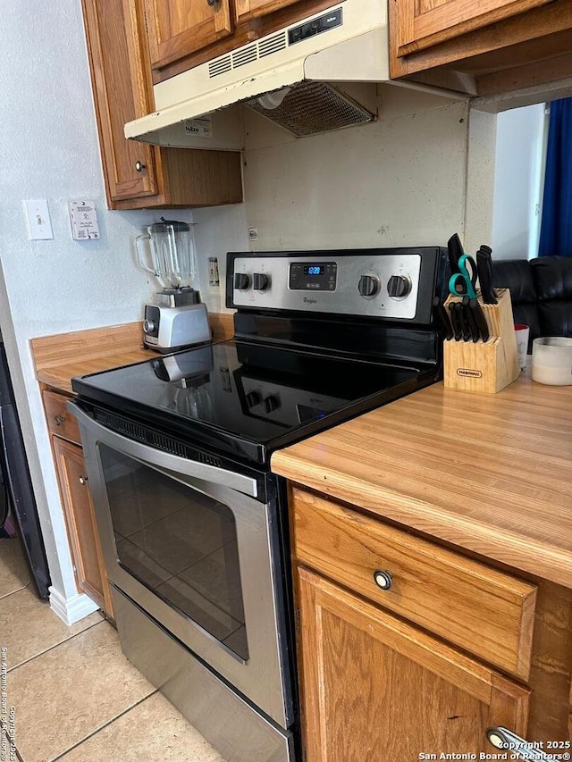 kitchen with under cabinet range hood, brown cabinetry, light tile patterned floors, wooden counters, and stainless steel electric stove