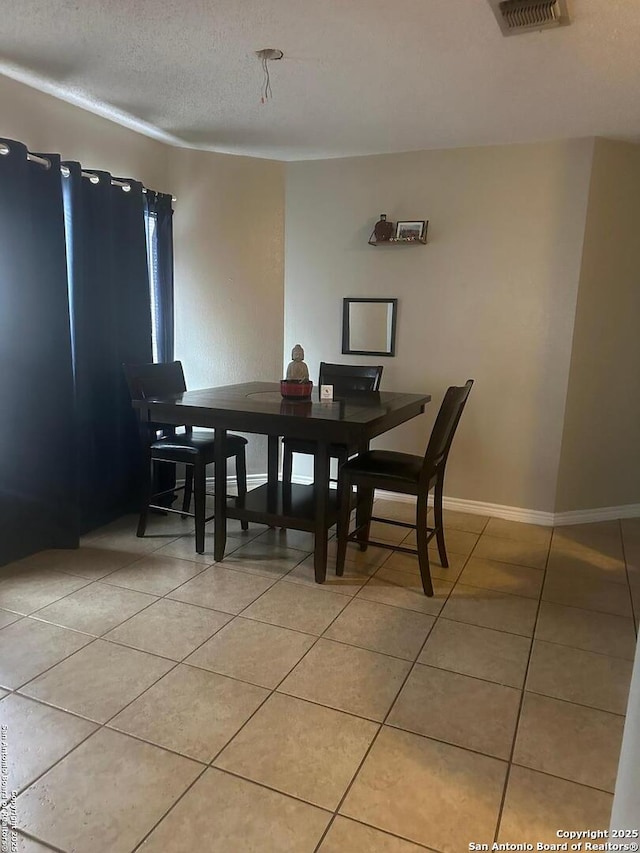 dining area featuring light tile patterned floors, baseboards, visible vents, and a textured ceiling