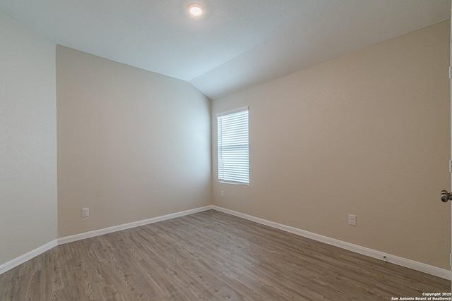 empty room featuring lofted ceiling, baseboards, and light wood-style floors