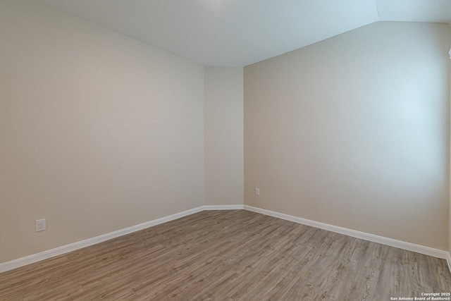 empty room with lofted ceiling, baseboards, and light wood-type flooring
