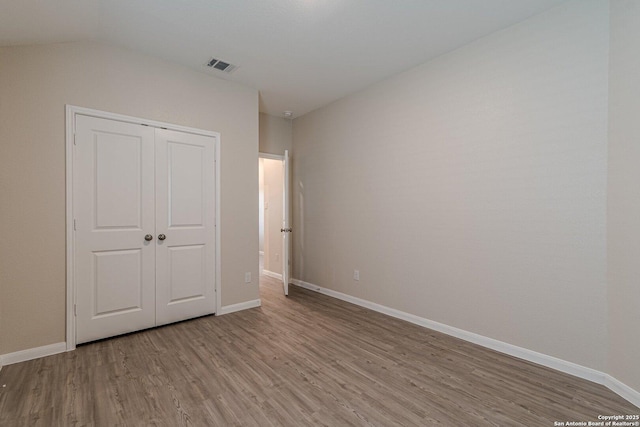 unfurnished bedroom with baseboards, a closet, visible vents, and wood finished floors