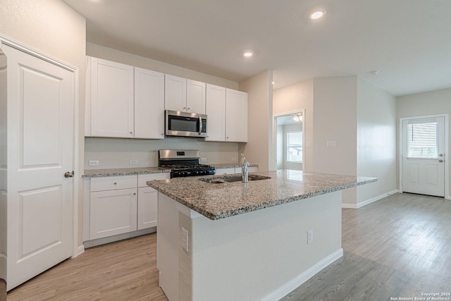 kitchen with white cabinets, appliances with stainless steel finishes, light stone countertops, and light wood-type flooring