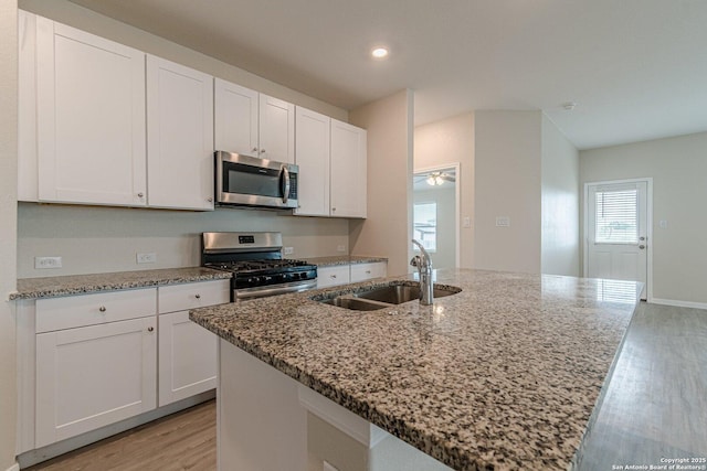 kitchen with a sink, light wood-style floors, white cabinets, and appliances with stainless steel finishes