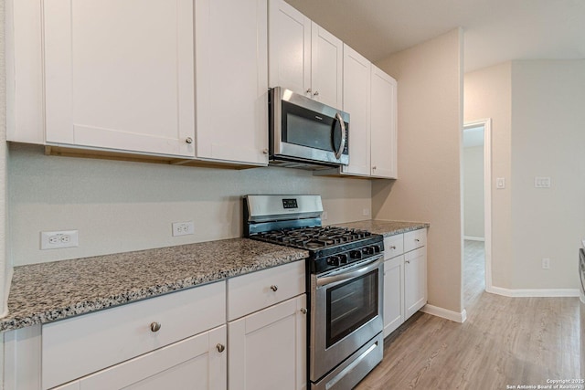 kitchen with light stone countertops, baseboards, white cabinetry, light wood-style floors, and stainless steel appliances