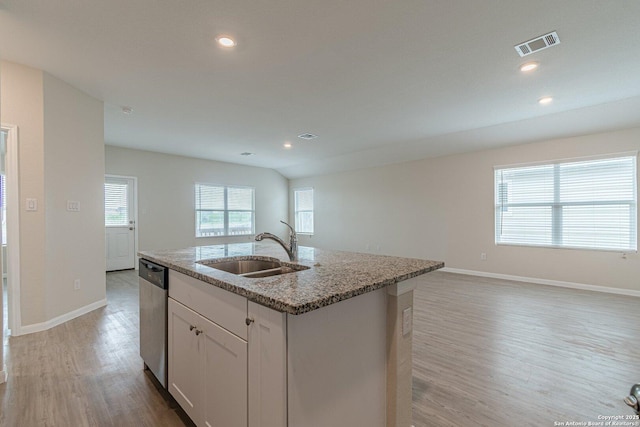 kitchen featuring a sink, light stone counters, a center island with sink, light wood-style flooring, and stainless steel dishwasher