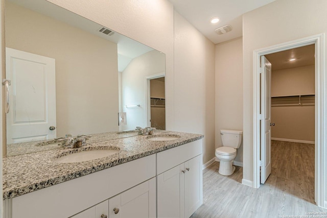 bathroom featuring toilet, visible vents, a sink, double vanity, and wood finished floors