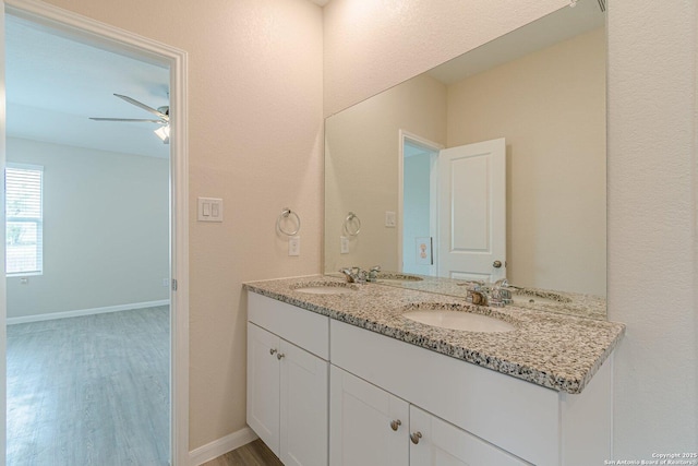 bathroom featuring a ceiling fan, double vanity, a sink, and wood finished floors