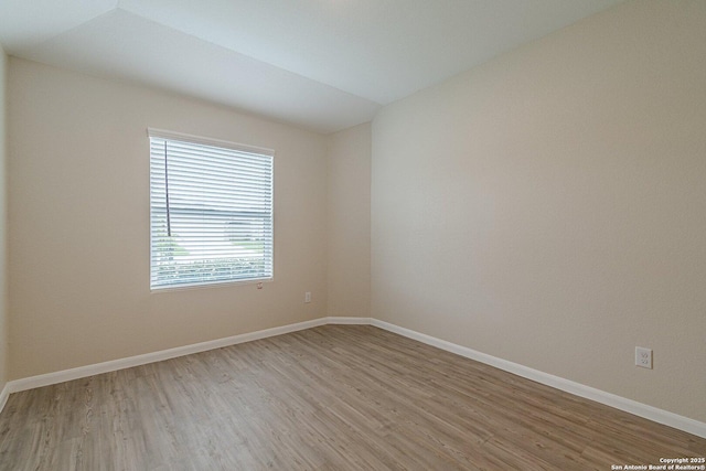 empty room featuring light wood-style flooring, baseboards, and lofted ceiling
