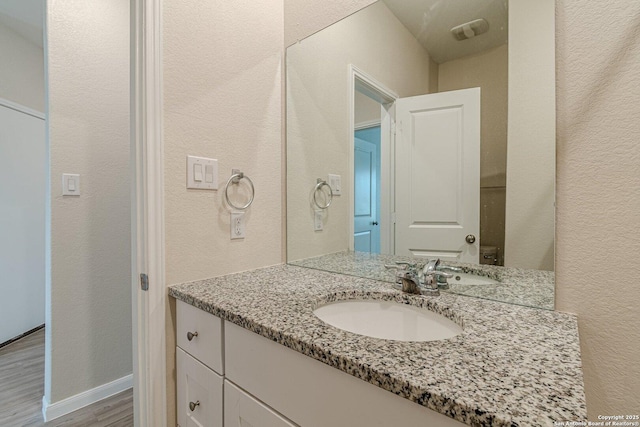 bathroom with wood finished floors, vanity, and a textured wall