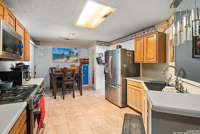 kitchen with a sink, brown cabinetry, a textured ceiling, light countertops, and appliances with stainless steel finishes