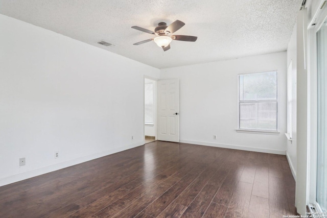 empty room with a textured ceiling, visible vents, ceiling fan, dark wood-style flooring, and baseboards