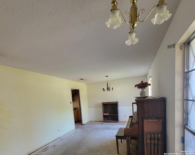 interior space featuring wallpapered walls, an inviting chandelier, concrete floors, and a textured ceiling