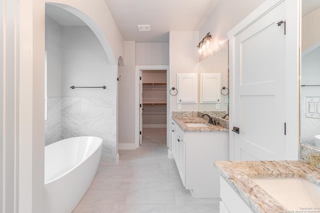 bathroom featuring a sink, two vanities, a freestanding tub, marble finish floor, and a spacious closet