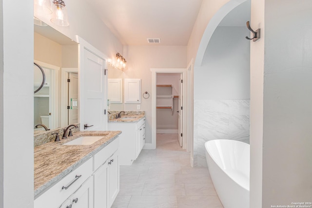bathroom with a freestanding bath, visible vents, a sink, and a walk in closet
