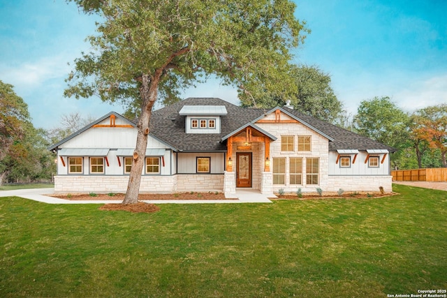 view of front of home featuring fence, a shingled roof, stone siding, and a front yard