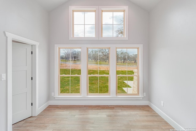 interior space featuring light wood finished floors, baseboards, and lofted ceiling