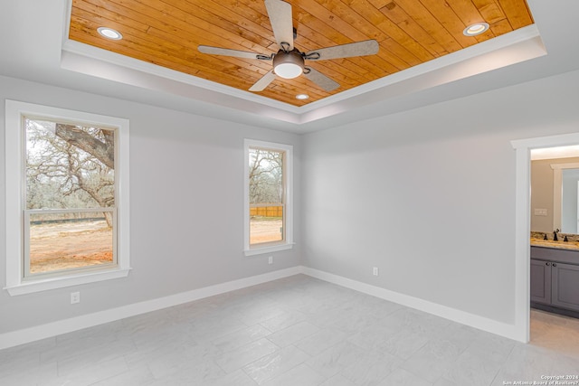 spare room with a sink, a ceiling fan, a tray ceiling, wood ceiling, and baseboards