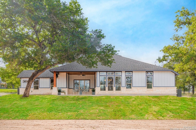 back of house featuring stone siding, ceiling fan, board and batten siding, a lawn, and a shingled roof