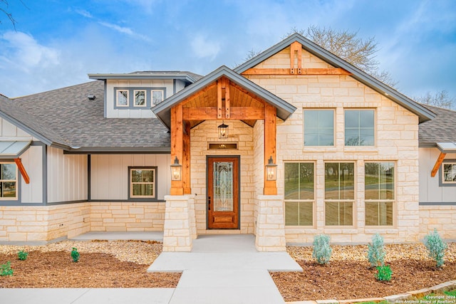 craftsman-style home with a shingled roof, stone siding, and board and batten siding
