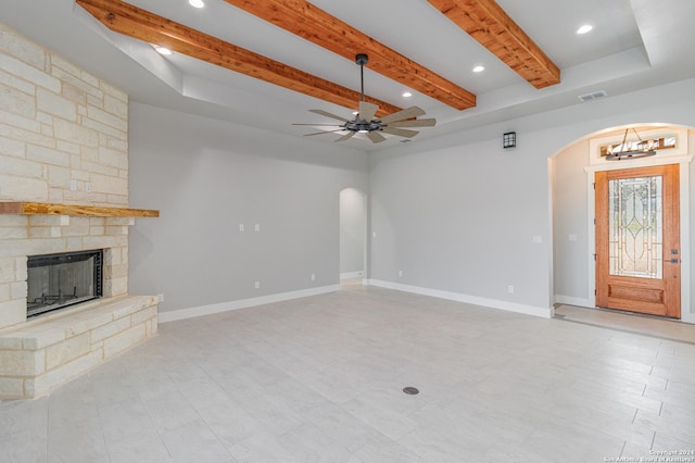 unfurnished living room featuring ceiling fan with notable chandelier, a fireplace, visible vents, beamed ceiling, and arched walkways