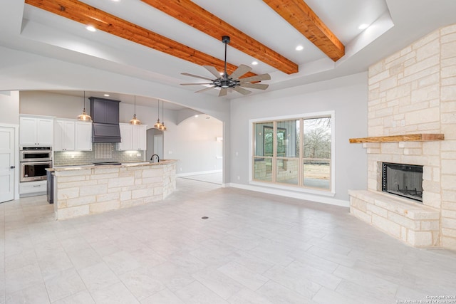 unfurnished living room featuring a ceiling fan, a sink, arched walkways, beamed ceiling, and a fireplace