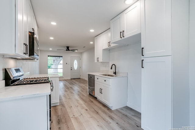 kitchen with a sink, light wood finished floors, a ceiling fan, baseboards, and appliances with stainless steel finishes