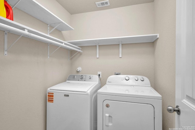 washroom with independent washer and dryer, visible vents, and laundry area