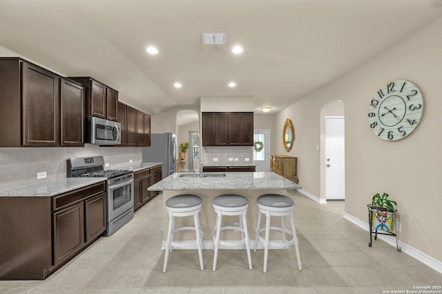kitchen featuring stainless steel appliances, backsplash, arched walkways, and baseboards