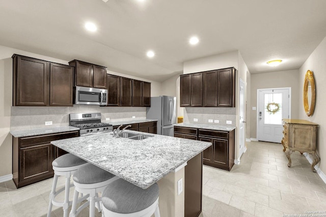 kitchen featuring baseboards, dark brown cabinets, a sink, tasteful backsplash, and appliances with stainless steel finishes