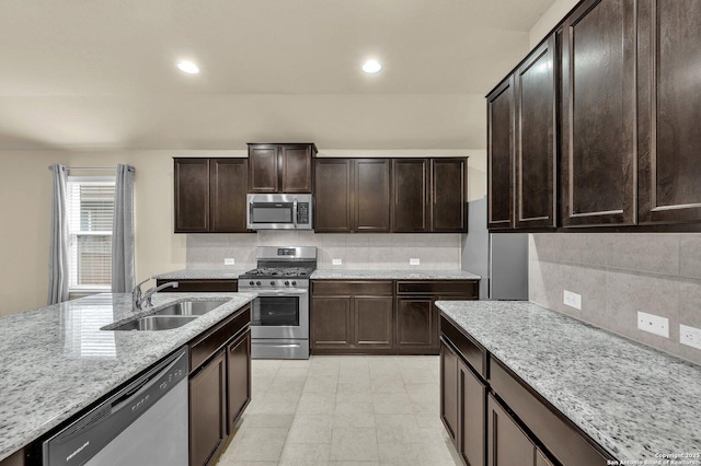kitchen with a sink, stainless steel appliances, tasteful backsplash, dark brown cabinetry, and light stone countertops