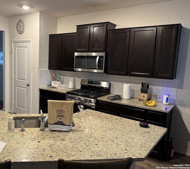 268 Cuban Emerald, San Antonio, TX 78253 - kitchen featuring a sink, tasteful backsplash, light stone counters, dark brown cabinetry, and appliances with stainless steel finishes