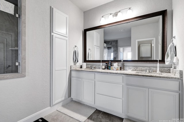 full bathroom featuring double vanity, baseboards, tile patterned flooring, a shower stall, and a textured wall