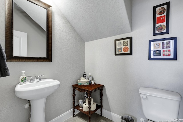 half bathroom featuring a sink, lofted ceiling, toilet, and baseboards