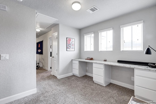 unfurnished office with built in desk, attic access, light colored carpet, and visible vents