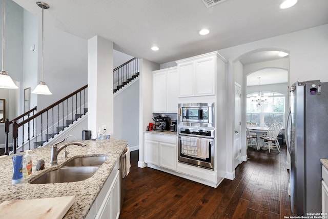 kitchen with a sink, dark wood finished floors, arched walkways, light stone countertops, and appliances with stainless steel finishes