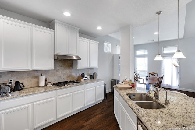 kitchen with under cabinet range hood, stainless steel gas stovetop, tasteful backsplash, a sink, and white cabinets