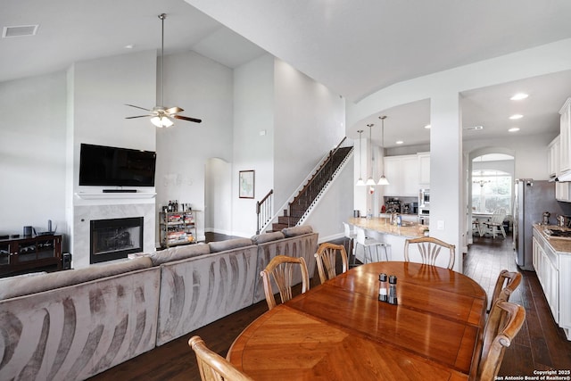 dining area featuring a fireplace, dark wood finished floors, ceiling fan, arched walkways, and stairs