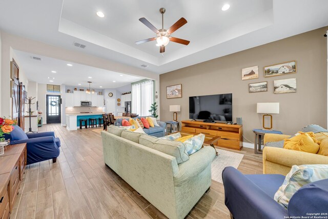living room with visible vents, a tray ceiling, ceiling fan, and light wood-style flooring