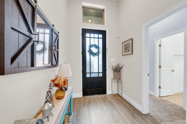 foyer entrance featuring a towering ceiling, plenty of natural light, wood finished floors, and baseboards