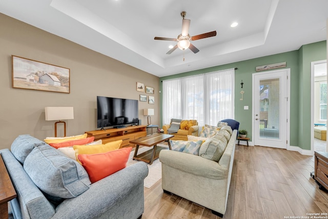 living area with a tray ceiling, ceiling fan, light wood-type flooring, and recessed lighting
