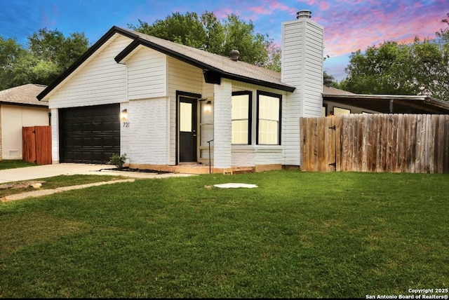 view of front facade with a chimney, fence, a lawn, brick siding, and driveway