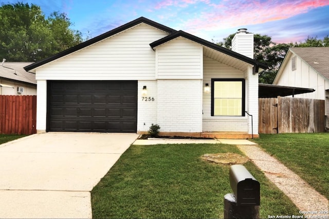 view of front of house featuring fence, brick siding, driveway, a front lawn, and a chimney