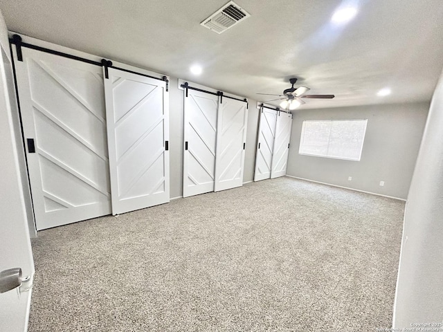 unfurnished bedroom with a barn door, baseboards, ceiling fan, visible vents, and carpet floors