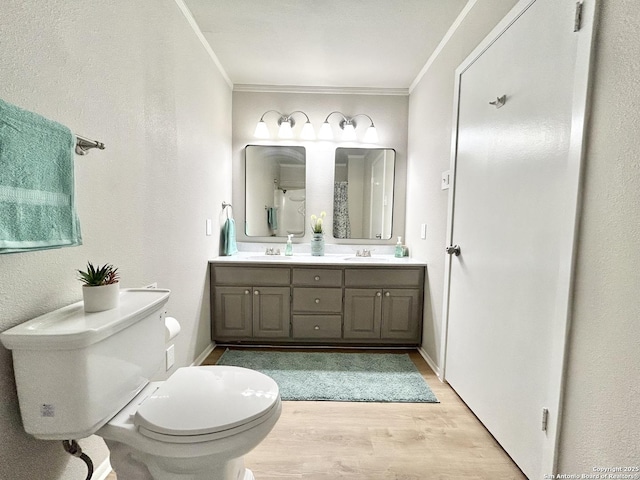 full bath featuring double vanity, toilet, wood finished floors, a sink, and crown molding