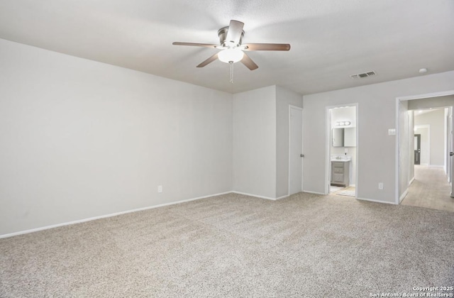 unfurnished bedroom featuring visible vents, baseboards, ceiling fan, light colored carpet, and ensuite bath