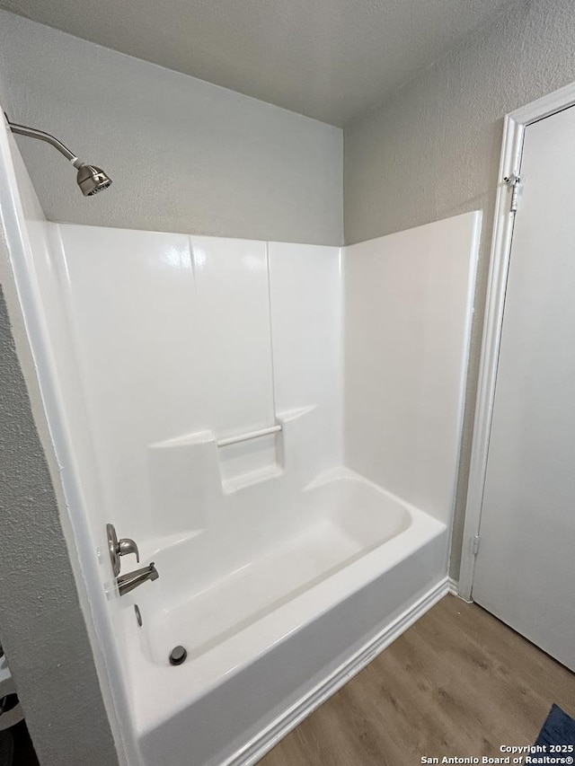 full bath featuring bathtub / shower combination, a textured wall, and wood finished floors