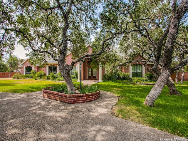 view of property hidden behind natural elements featuring french doors, brick siding, and a front yard