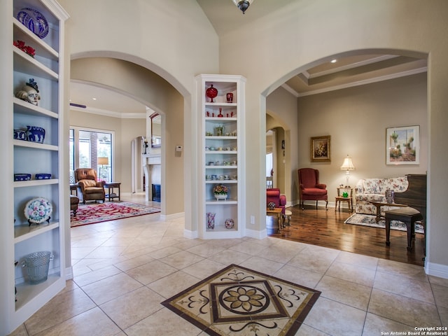 entryway with crown molding, baseboards, a towering ceiling, arched walkways, and light tile patterned flooring